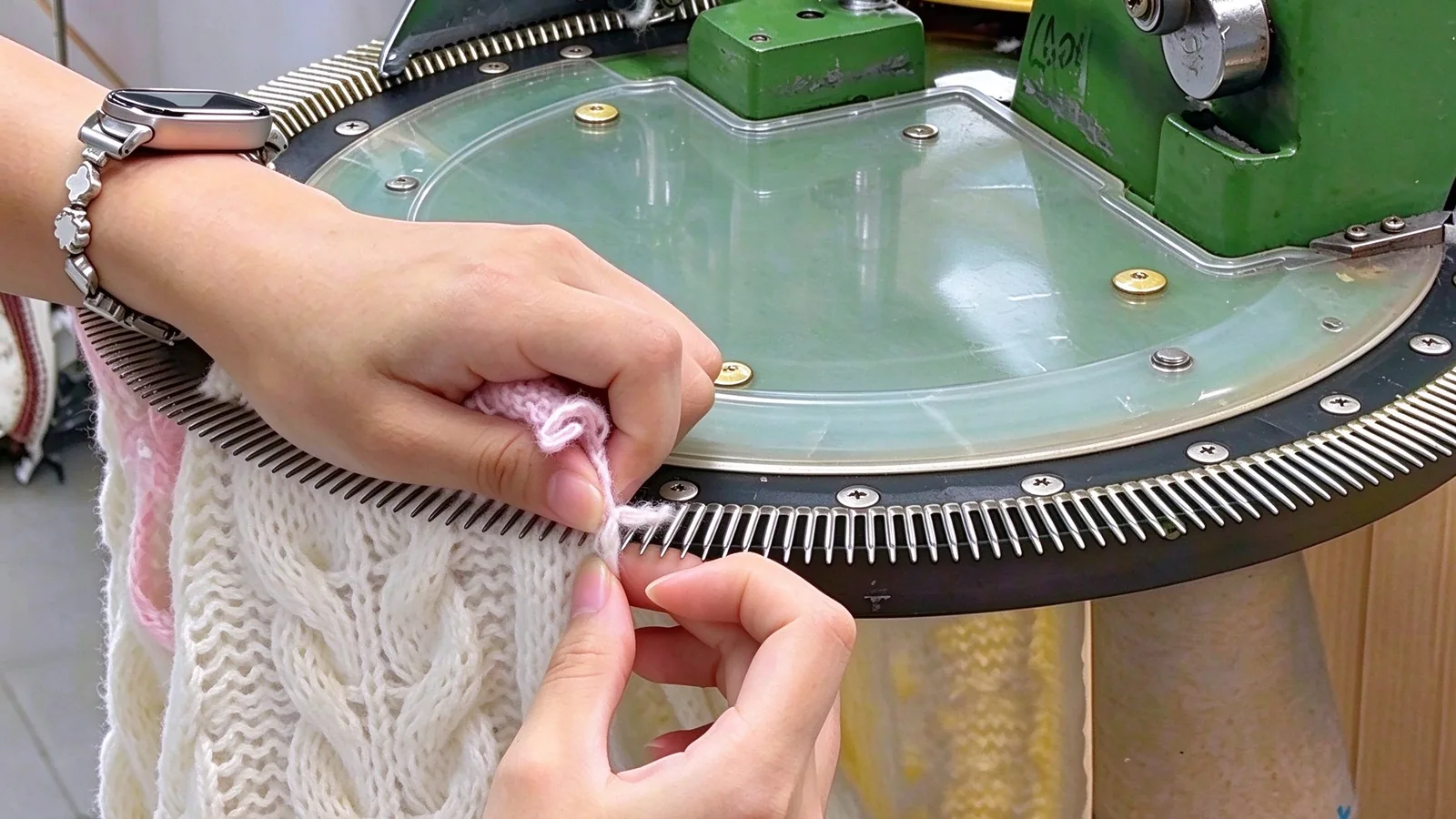 Hands feeding yarn onto a knitting machine needle bed